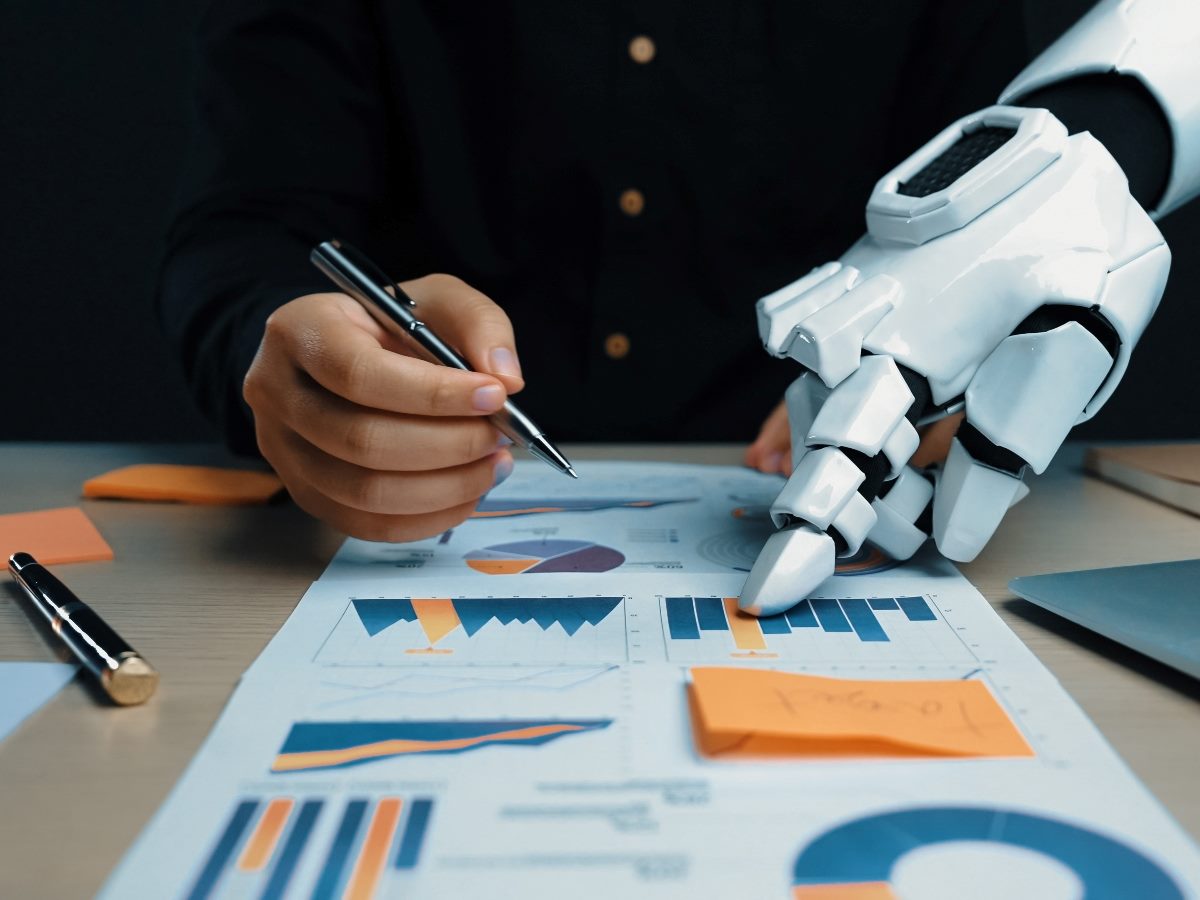 A scene depicting a robotic hand assisting a human in analyzing business charts and graphs.