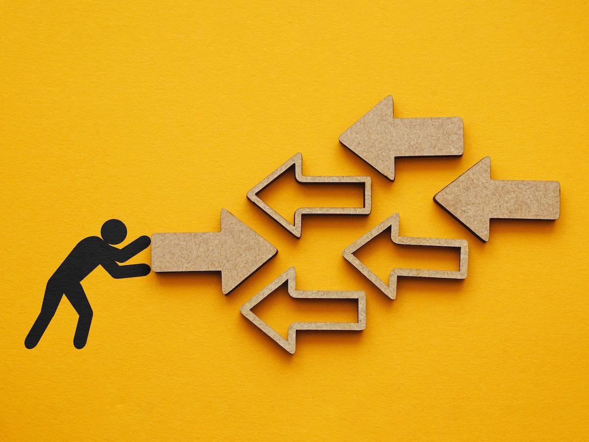 A figure of a person pushing an arrow towards several other arrows pointed in the opposite direction