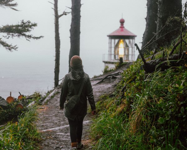 A person walks on a trail near a lighthouse and the Pacific Ocean.