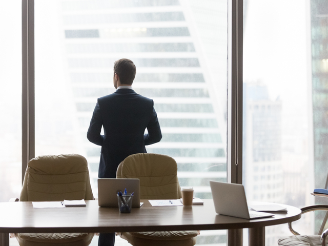 Rear view of contemplative businessman in modern office, looking out the window thinking of future business challenges - leadership concept