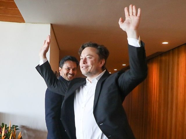Elon Musk with his hands raised and smiling with an unidentified man behind him.
